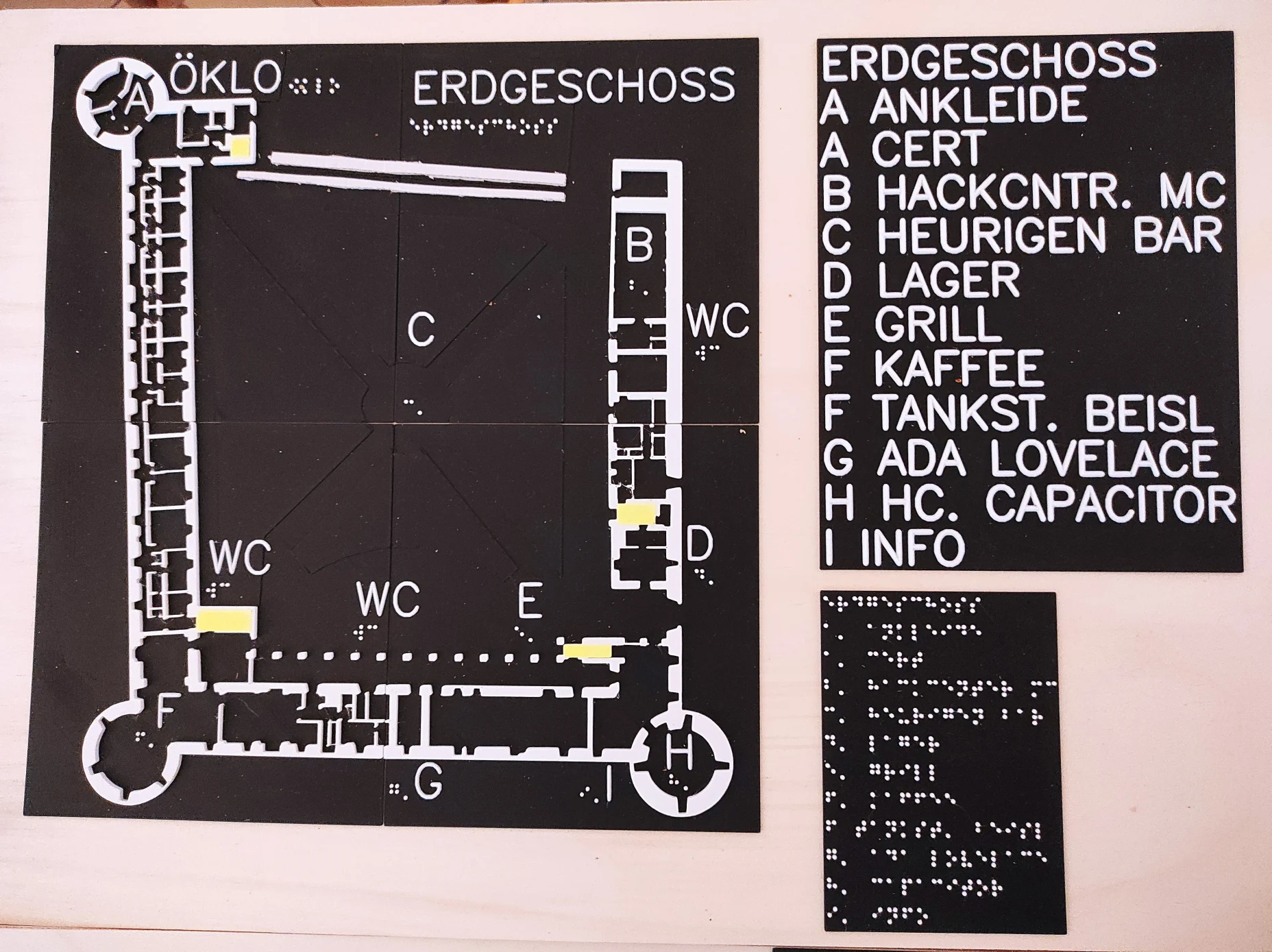 Weiße Schrift und Zeichnung auf drei schwarzen Platten. Platte mit Grundriss von einem Schloss mit drei runden Ecktürmen wird ergänzt von einer Legende in Profilschrift und einer Legende in Brailleschrift.